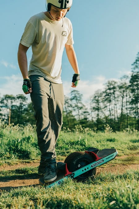A rider getting ready to ride a onewheel on dirt with all his safety gear on.